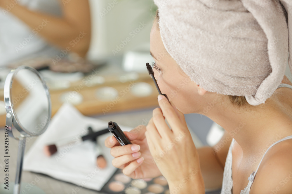 pretty young woman with towel on head applying mascara