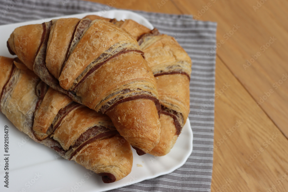 Many sweet croissants with chcolate on a white ceramic tray on wooden table