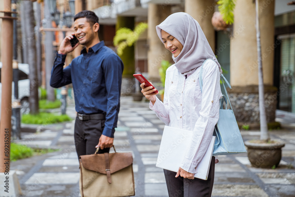 Asian woman in hijab using cell phone near businessman calling with outdoor background