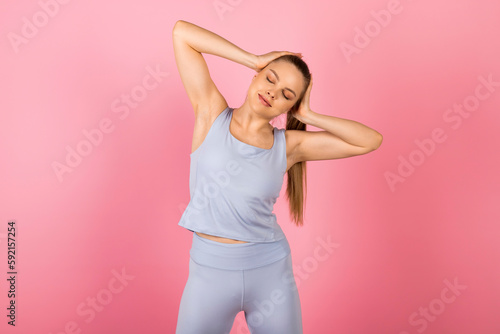 Young healthy Girl in gray sportswear is doing stretches and warm-up exercises. Isolated on pink background.