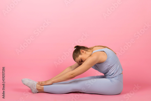 Young healthy Girl in gray sportswear is doing stretches and warm-up exercises. Isolated on pink background.