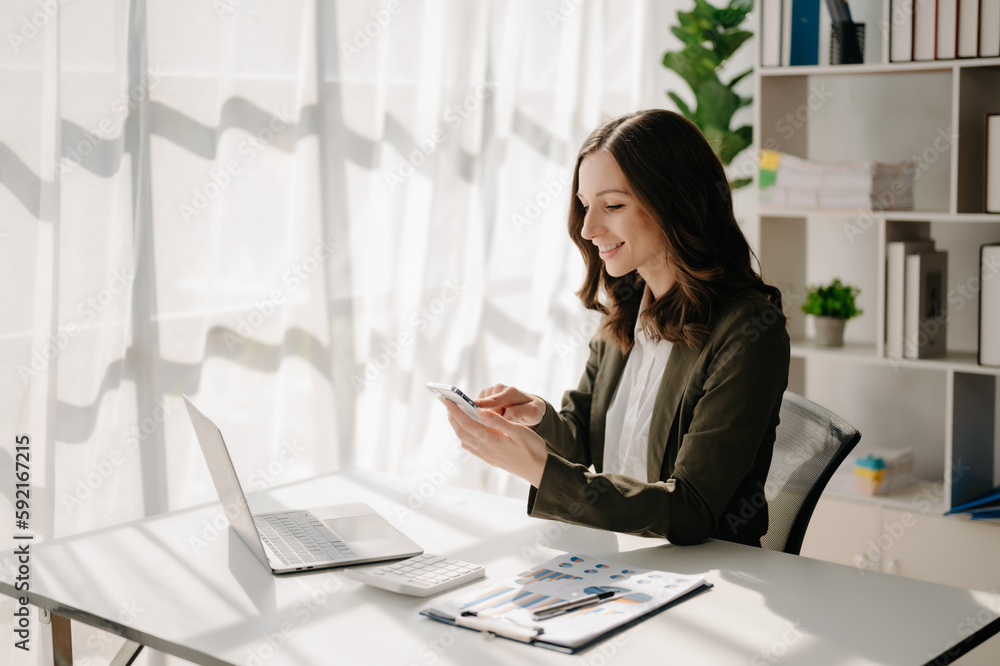Confident business expert attractive smiling young woman typing laptop ang holding digital tablet on desk in creative home office. Confident business expert attractive smiling young woman typing laptop ang holding digital tablet on desk in creative home office.