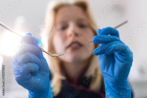 Close up, patients view of a dentist. Beautiful dentist in surgical gloves is holding tools and looking at camera