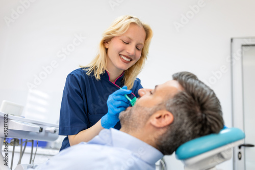 Female dentist treating teeth to patient, mid age man in chair at dental clinic. Dentistry, healthy teeth, medicine and healthcare concept