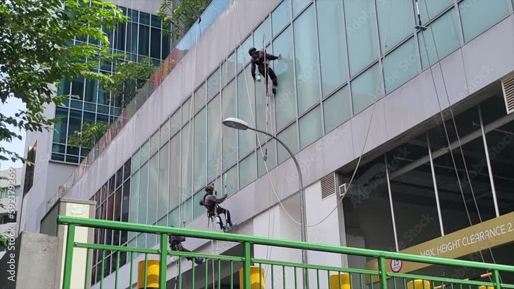 Cleaners Hanging By The Ropes Cleaning And Washing The Exterior Wall Of A High-rise Building In The City. - static Cleaners Hanging By The Ropes Cleaning And Washing The Exterior Wall Of A High-rise Building In The City. - static