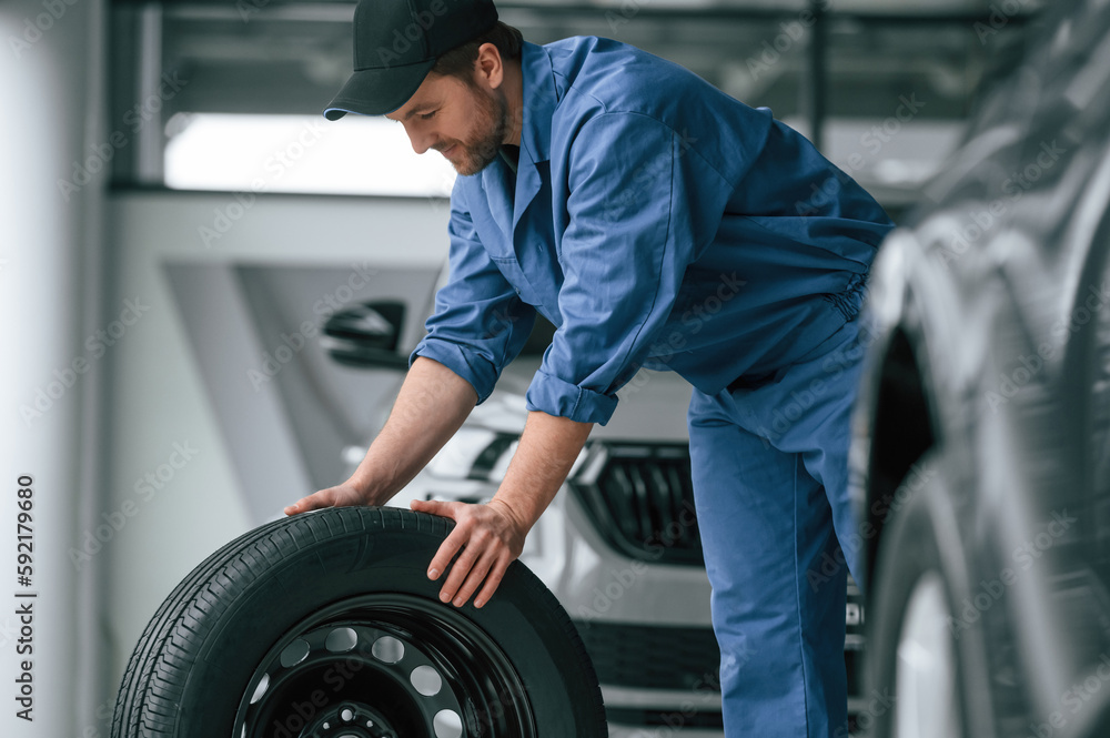 Moving the tire. Man in blue uniform is working in the car service