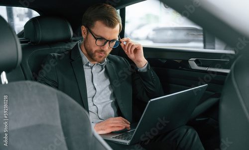 With laptop, working. Man in formal business clothes is sitting in the modern automobile © standret
