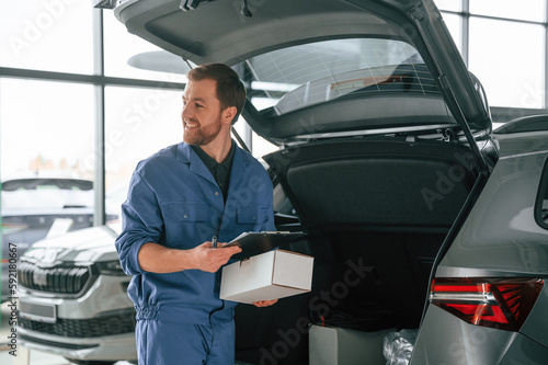 White box and notepad in hands. Man in blue uniform is working in the car service
