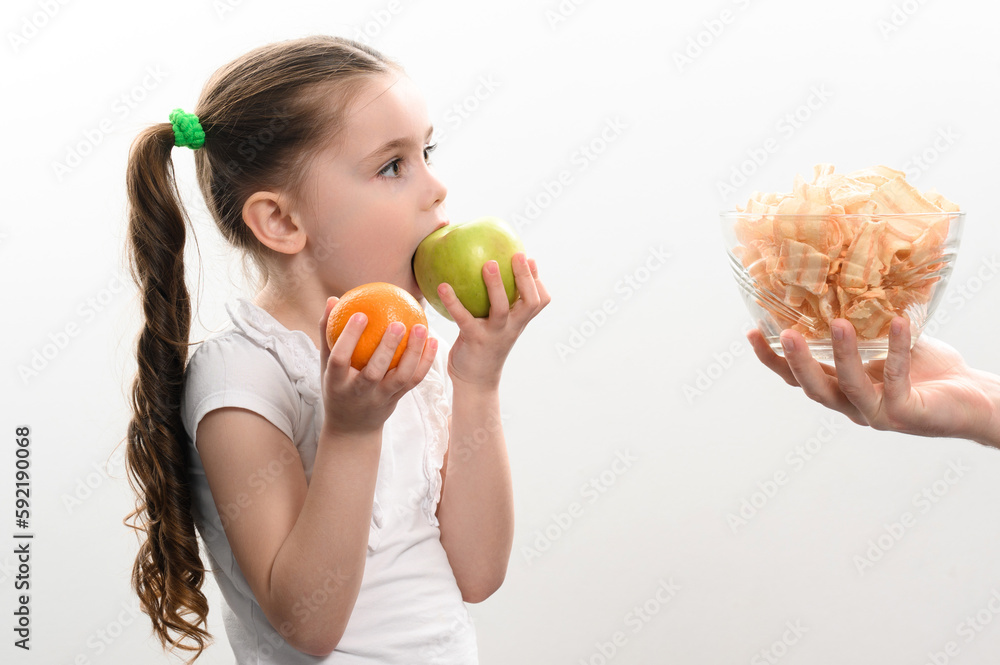 Big bowl of chips and fruit, beautiful little girl eats an apple, child is given a bowl of chips, white background and copy space. Big bowl of chips and fruit, beautiful little girl eats an apple, child is given a bowl of chips, white background and copy space.