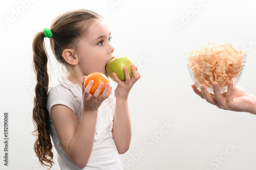 Big bowl of chips and fruit, beautiful little girl eats an apple, child is given a bowl of chips, white background and copy space.