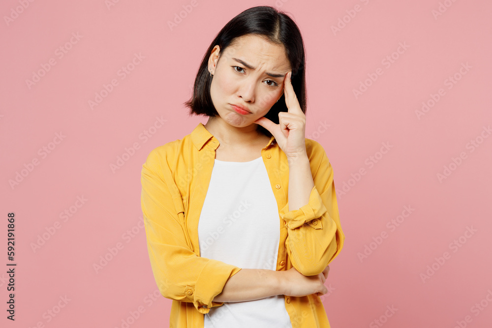 Young sad upset dissatisfied woman of Asian ethnicity wears yellow shirt white t-shirt look camera prop up forehead isolated on plain pastel light pink background studio portrait. Lifestyle concept. Young sad upset dissatisfied woman of Asian ethnicity wears yellow shirt white t-shirt look camera prop up forehead isolated on plain pastel light pink background studio portrait. Lifestyle concept.