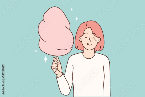 Cheerful girl with cotton candy in hands licks lips in anticipation taste of street dessert 