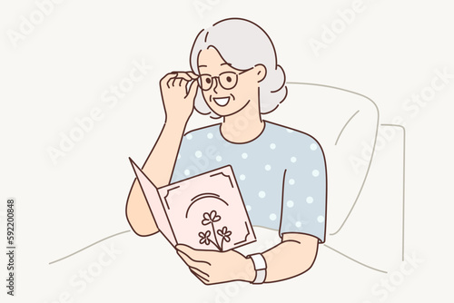 Sick elderly woman lying in hospital holds card from loved ones with wishes for speedy recovery 