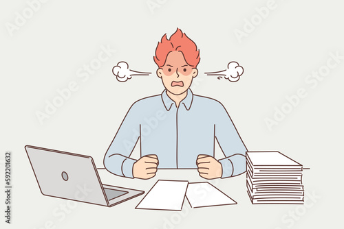 Angry man suffering from overwork and paperwork sitting at office desk with laptop