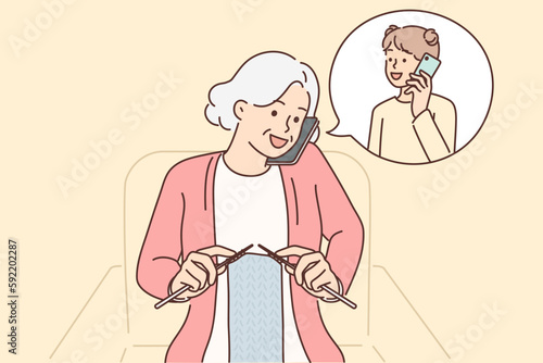 Grandmother makes phone call to granddaughter and knits scarf sitting in cozy chair