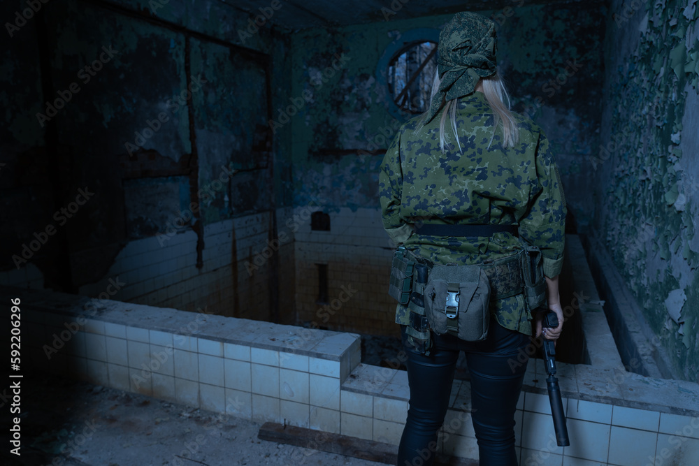 Soldier girl in uniform with a pistol with a silencer in a ruined building with a swimming pool, view from the back, low lighting from the moonlight.