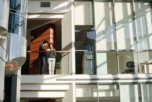 Young business people using digital tablet together while standing on balcony of modern office building