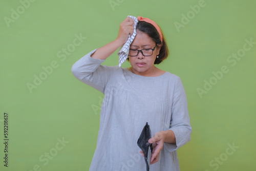 A woman was holding an empty wallet while wiping the sweat off her forehead; nervous expression. photo