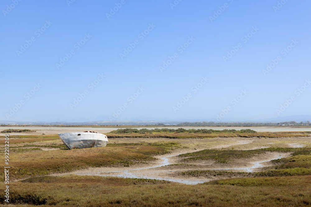 Paisaje del litoral gaditano, con una barca abandonada al bajar la marea, sobre las marismas con un cielo azul despejado. Paisaje del litoral gaditano, con una barca abandonada al bajar la marea, sobre las marismas con un cielo azul despejado.