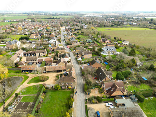 Drone view of a typical main road interesting an English village. A large Manor House and gardens are seen on the left.