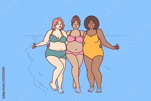 Cheerful plus size women dressed in swimsuit stand hugging on sunny beach near sea water and look at camera smiling. Diverse plus size girls for concept of no prejudice and body positivity