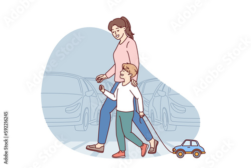 Happy mom and child going along pedestrian crossing across road walking through summer city. Little boy with toy car walks with nanny teaching how to cross intersection road correctly 