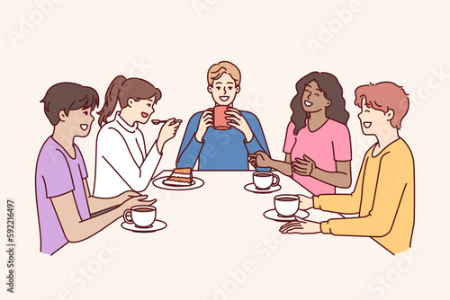 Group of multiethnic colleagues drink coffee sitting at table during break and laugh telling funny jokes. Happy people in casual wear relaxing enjoying socializing and meeting with school friends 
