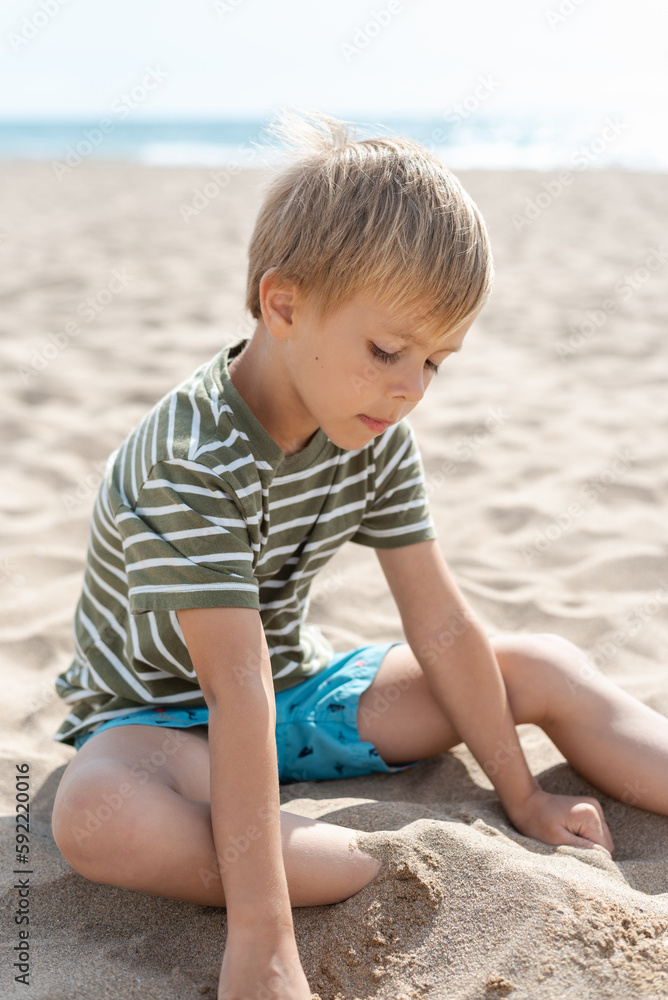 Candid portrait of a pensive little boy sitting on a sandy beach