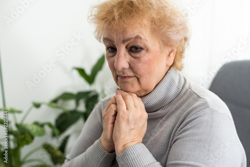 Elderly woman keeps palms in pray gesture, closes eyes, prays and asks God for health and wellness. Faith generation concept