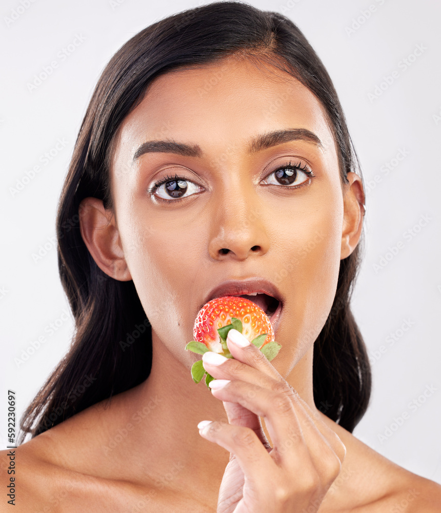 Portrait, beauty and a woman biting a strawberry in studio on a gray background for health, diet or nutrition. Face, skincare and serious with an attractive young female model eating a fruit berry Portrait, beauty and a woman biting a strawberry in studio on a gray background for health, diet or nutrition. Face, skincare and serious with an attractive young female model eating a fruit berry