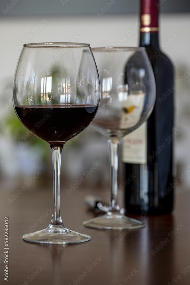 Vertical of one half filled and another empty wine glasses in front of a wine bottle on a table