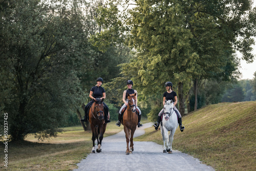 Three female riders riding horses along the trail by the river. Recreation and leisure activity concepts. © 24K-Production