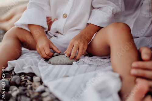 A small child, a girl in a white dress, plays with sea stones that she holds in her hands © Ilya.K