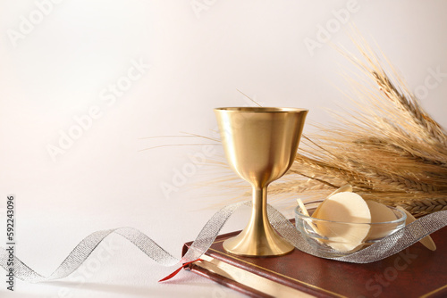 Foto Cup and hosts on bible with ribbon and wheat ears