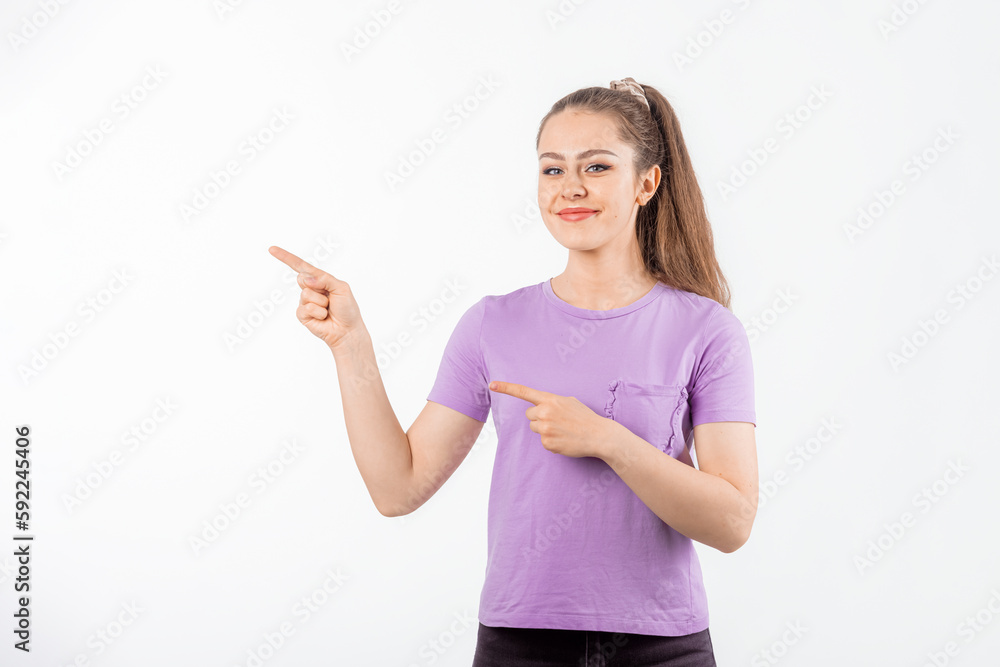 Smiling young woman with long hair points fingers at banner, shows great promo offer aside, stands in casual t shirt over white background Smiling young woman with long hair points fingers at banner, shows great promo offer aside, stands in casual t shirt over white background