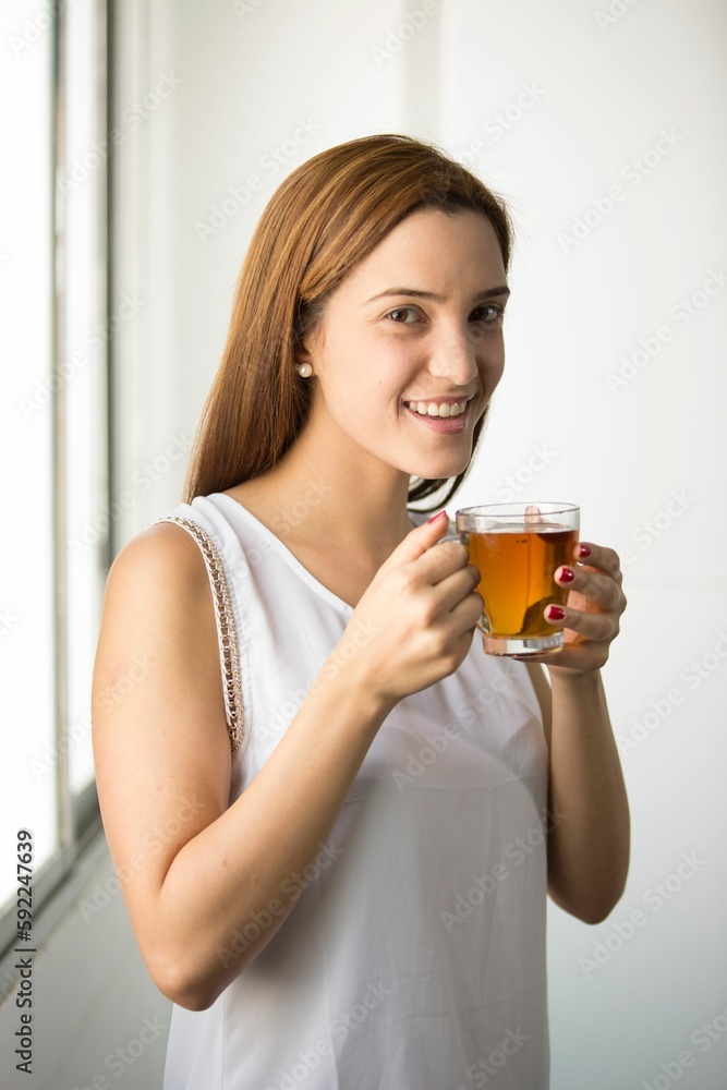 Woman holding glass of tea and looking at camera with smile in white background Woman holding glass of tea and looking at camera with smile in white background