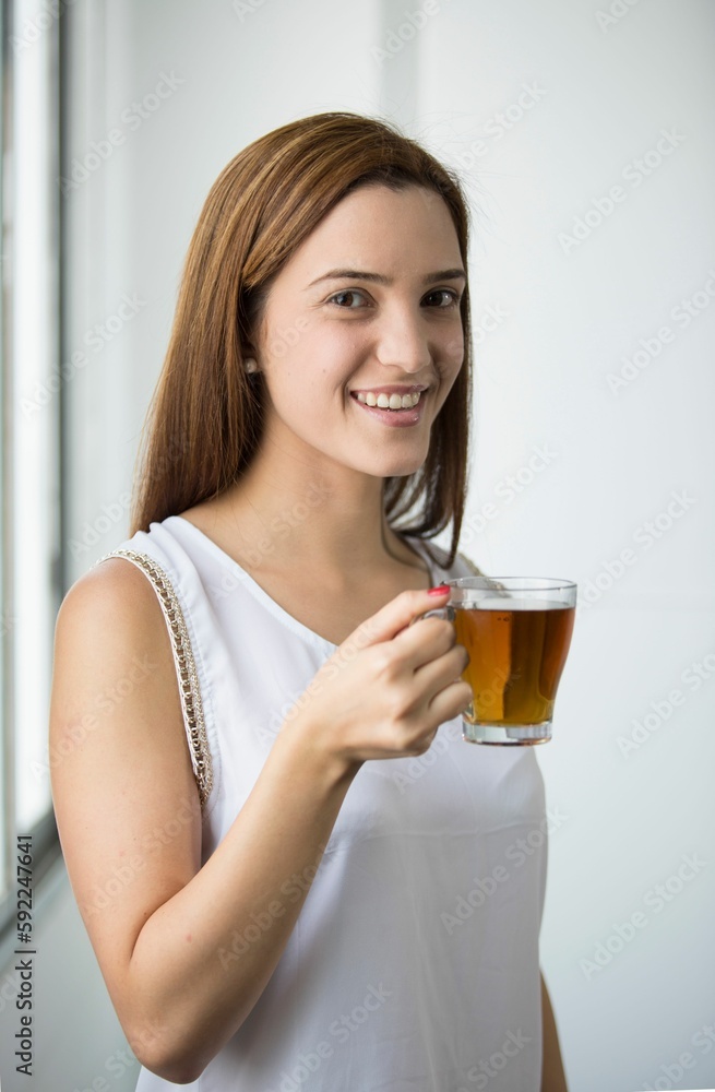 Woman holding glass of tea and looking at camera with smile in white background Woman holding glass of tea and looking at camera with smile in white background
