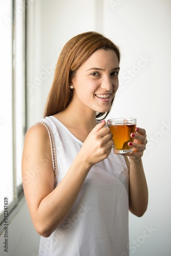 Woman holding glass of tea and looking at camera with smile in white background