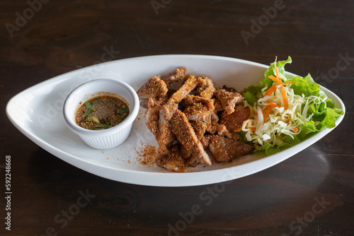Delicious Thai-style grilled pork with chili powder and roasted rice served with Thai-style dipping sauce and lettuce on a white plate on a black table.