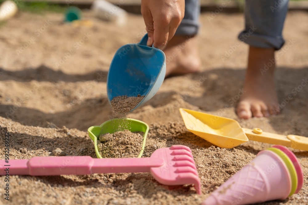 Child playing with the sand at the beach with colorful shovels Child playing with the sand at the beach with colorful shovels