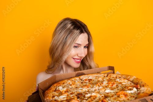 A beautiful fit young blonde girl with a big open pizza box. Isolated on yellow.