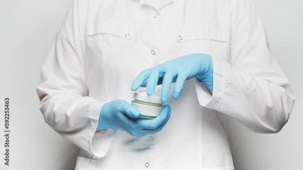 Woman in a white lab coat and blue gloves taking the lid off of a jar of face cream, showing its content. Close up, slow motion, 4k. Woman in a white lab coat and blue gloves taking the lid off of a jar of face cream, showing its content. Close up, slow motion, 4k.