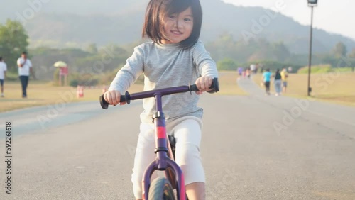 Little asian girl riding bike along the outdoor road, summer outdoor activity, open area for kids playground, enjoy ride a bike, kids playtime for good emotion, child growth hormones, fun and friendly