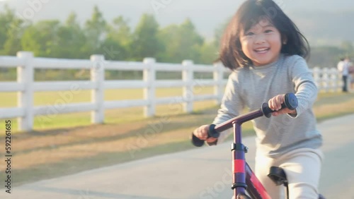 Happy cheerful little asian girl balancing bike running along the outdoor road, summer outdoor activity, kids playground, enjoy ride a bike, kids playtime for good emotion, child growth hormones, 