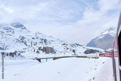 Bernina mountain pass. The famous red train is crossing the white lake. Amazing landscape of the Switzerland land. Famous destination and tourists attraction