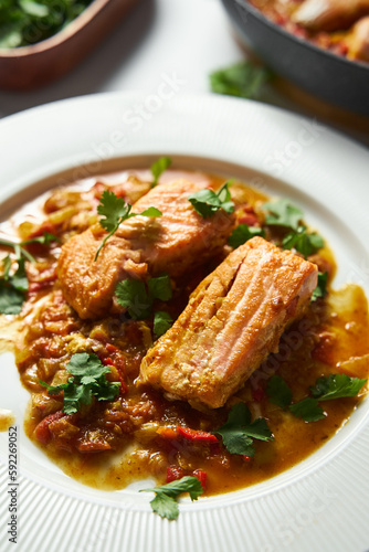 Indian red salmon curry with tomatoes. Asian Cuisine. Tomato-infused Red Salmon Curry and Fried Vegetables with Green Cilantro. Close up. Vertical photo 