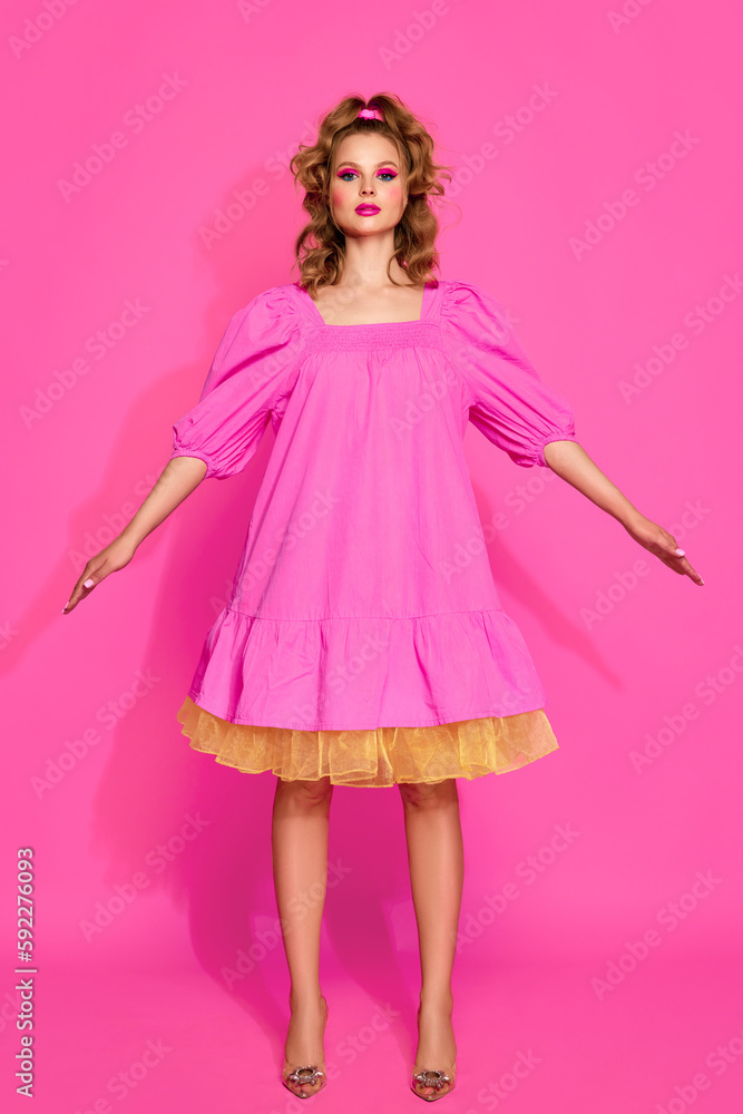 One stunning blond woman, girl with bright makeup wearing doll dress and heels posing over pink studio background. Blank face One stunning blond woman, girl with bright makeup wearing doll dress and heels posing over pink studio background. Blank face