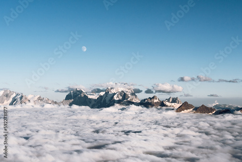View of the moon and the Caucasian ridge with Mount Ushba above the clouds © Maksim