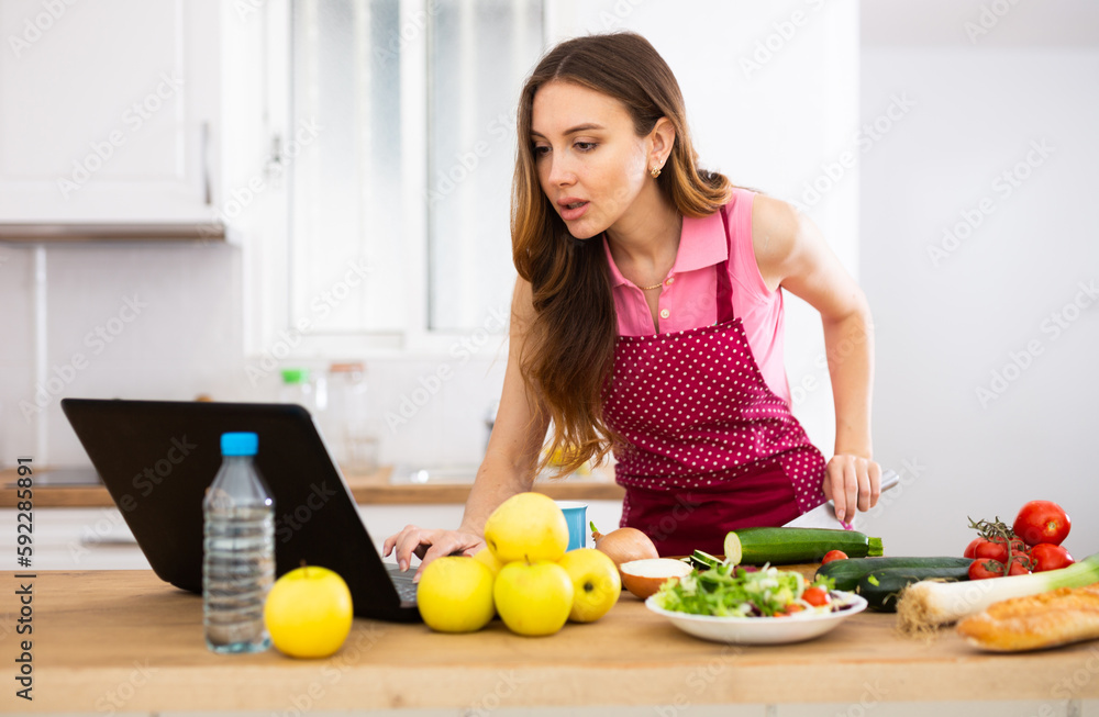 Woman cook reads the recipe in laptop and cooks salad in kitchen