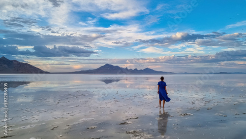 Silhouette of woman walking into the sunset of lake Bonneville Salt Flats, Wendover, Western Utah, USA, America. Beautiful summits of Silver Island Mountain range reflecting in water surface. Awe